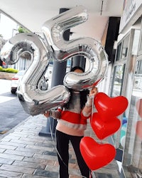 a woman holding a silver heart balloon with the number 25