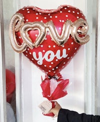 a person holding a heart shaped foil balloon that says love you