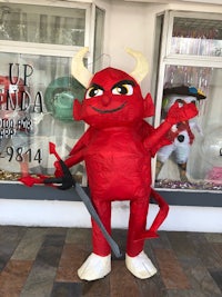 a red devil mascot standing in front of a store