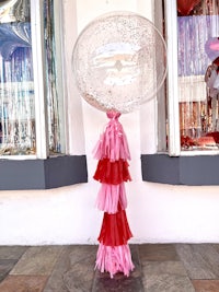 a pink and red balloon with tassels in front of a store