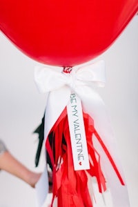 a person holding a red balloon with a ribbon tied around it