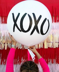 a woman holding up a balloon with the word xoxo written on it