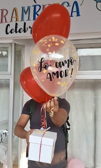 a man holding a box of balloons and a gift