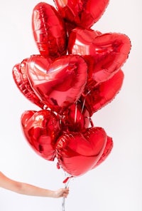 a woman holding a bunch of red heart balloons